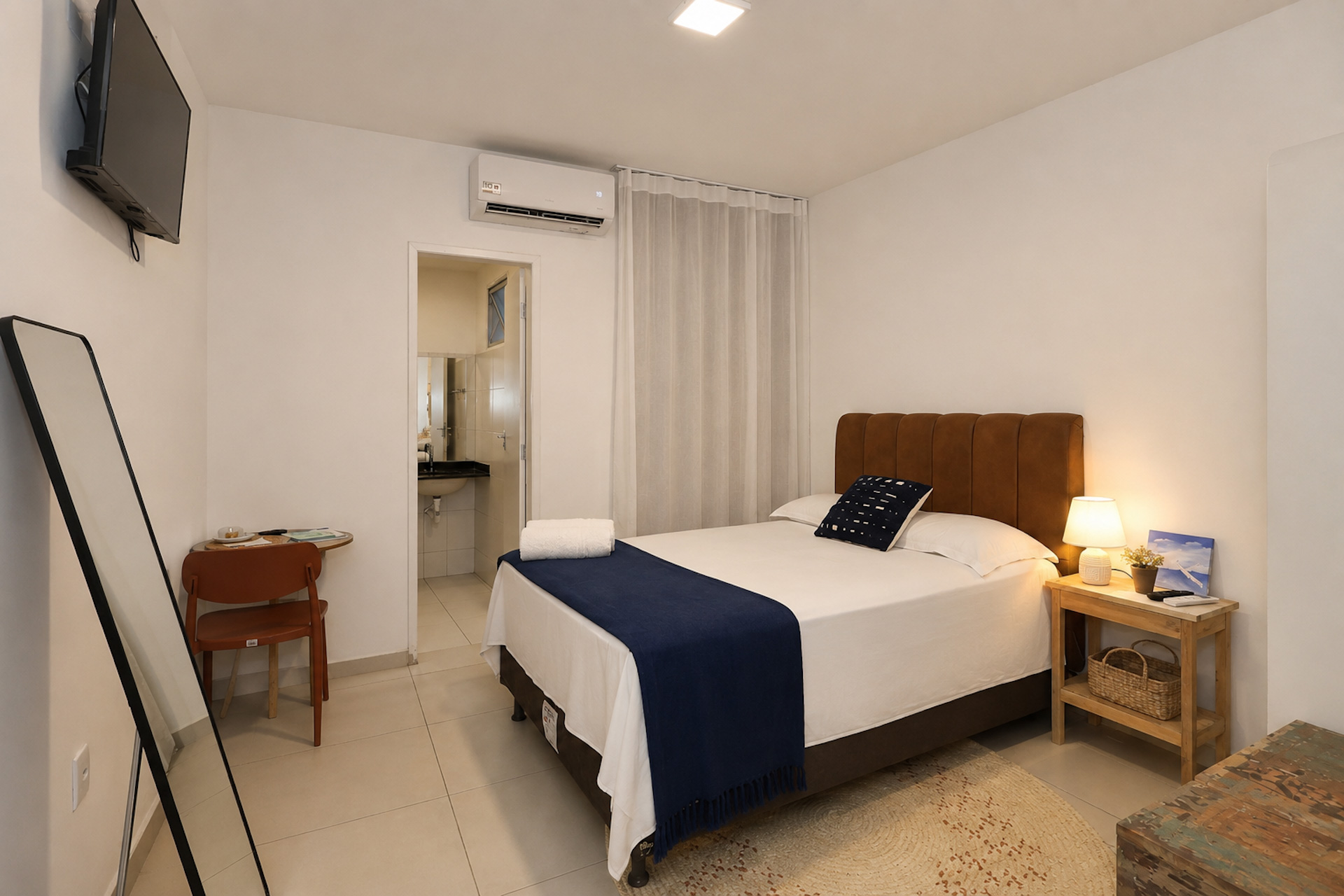 Quarto de casal com manta azul-marinho, espelho de corpo inteiro e porta ao fundo