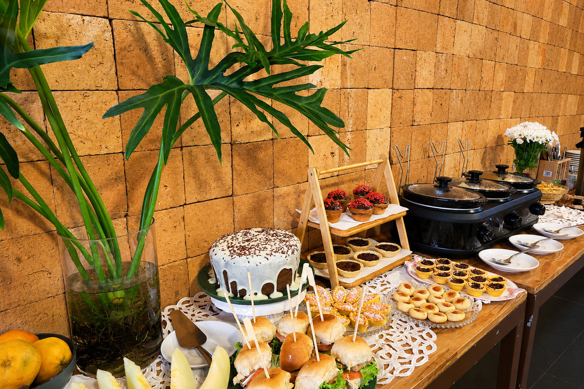 Mesa farta de café da manhã com bolos, tortinhas e frutas, sobre parede de pedra