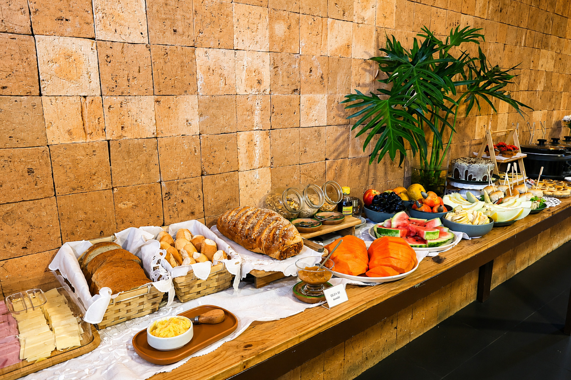 Cesta de pães, queijos e frutas sobre parede de ripas de madeira