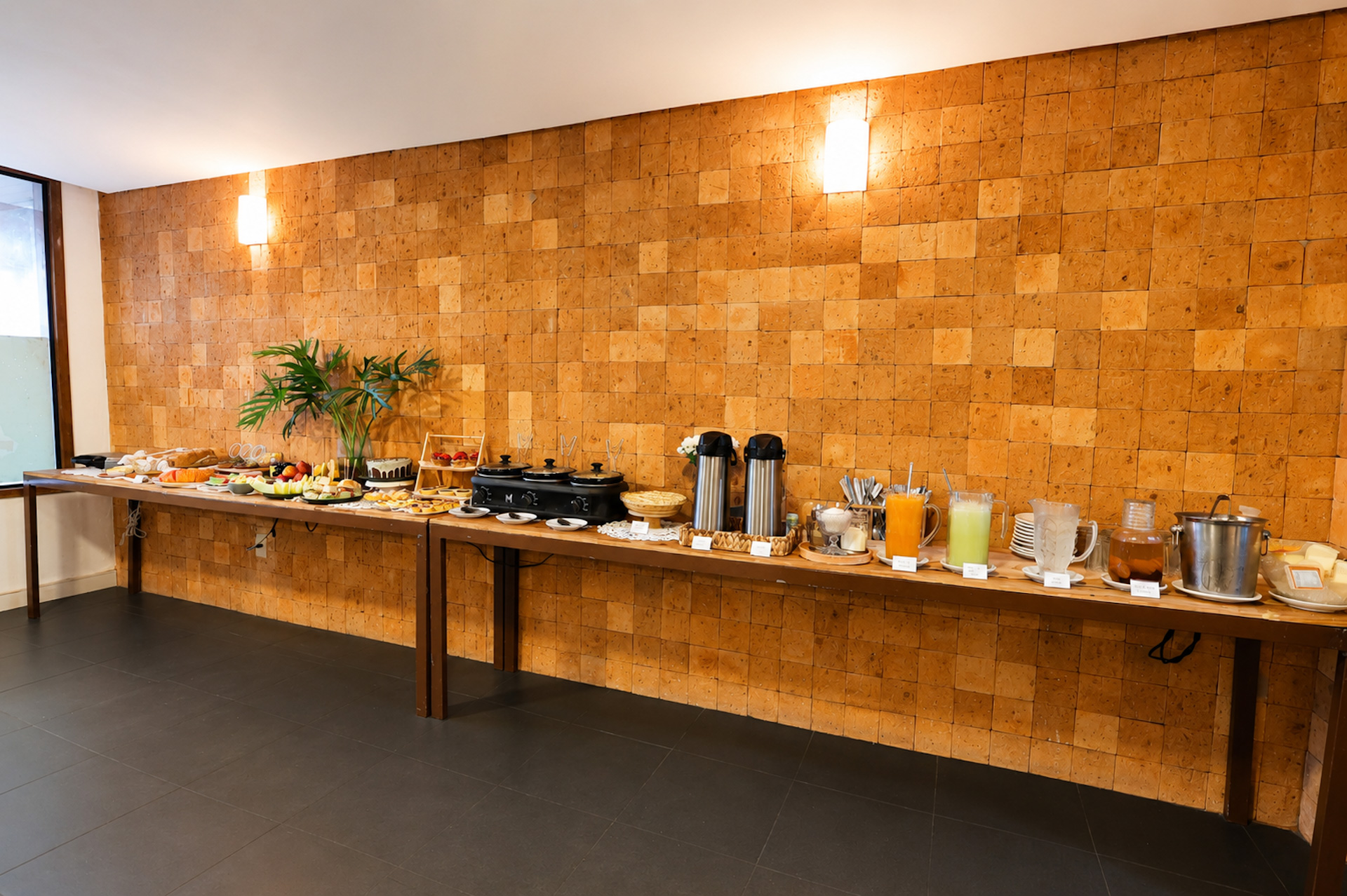 Buffet de café da manhã com garrafas térmicas e xícaras sobre parede de cortiça