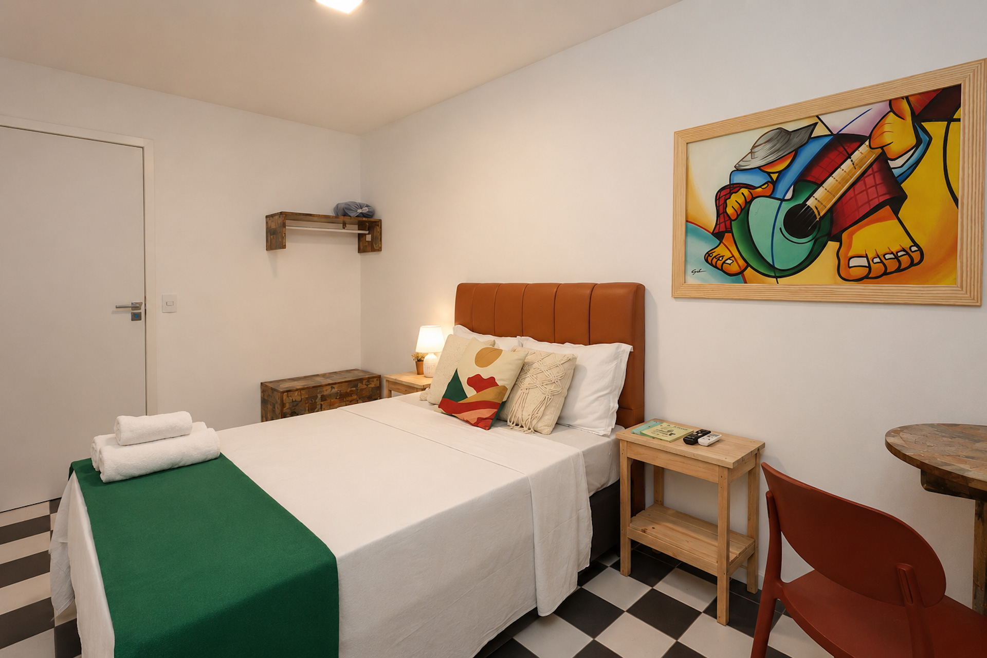 Quarto de casal com manta verde, quadro colorido e piso xadrez preto e branco