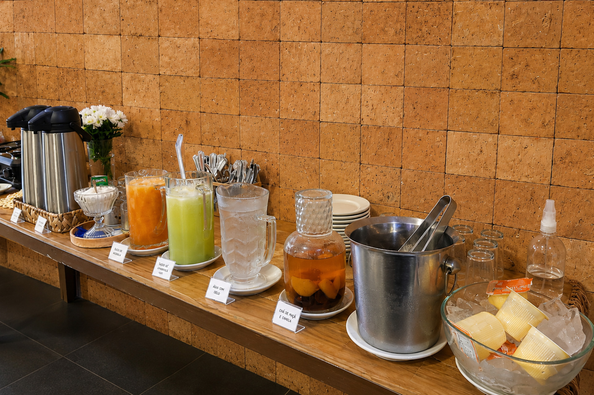 Buffet de café da manhã com garrafas térmicas, sucos, granola e frutas em calda