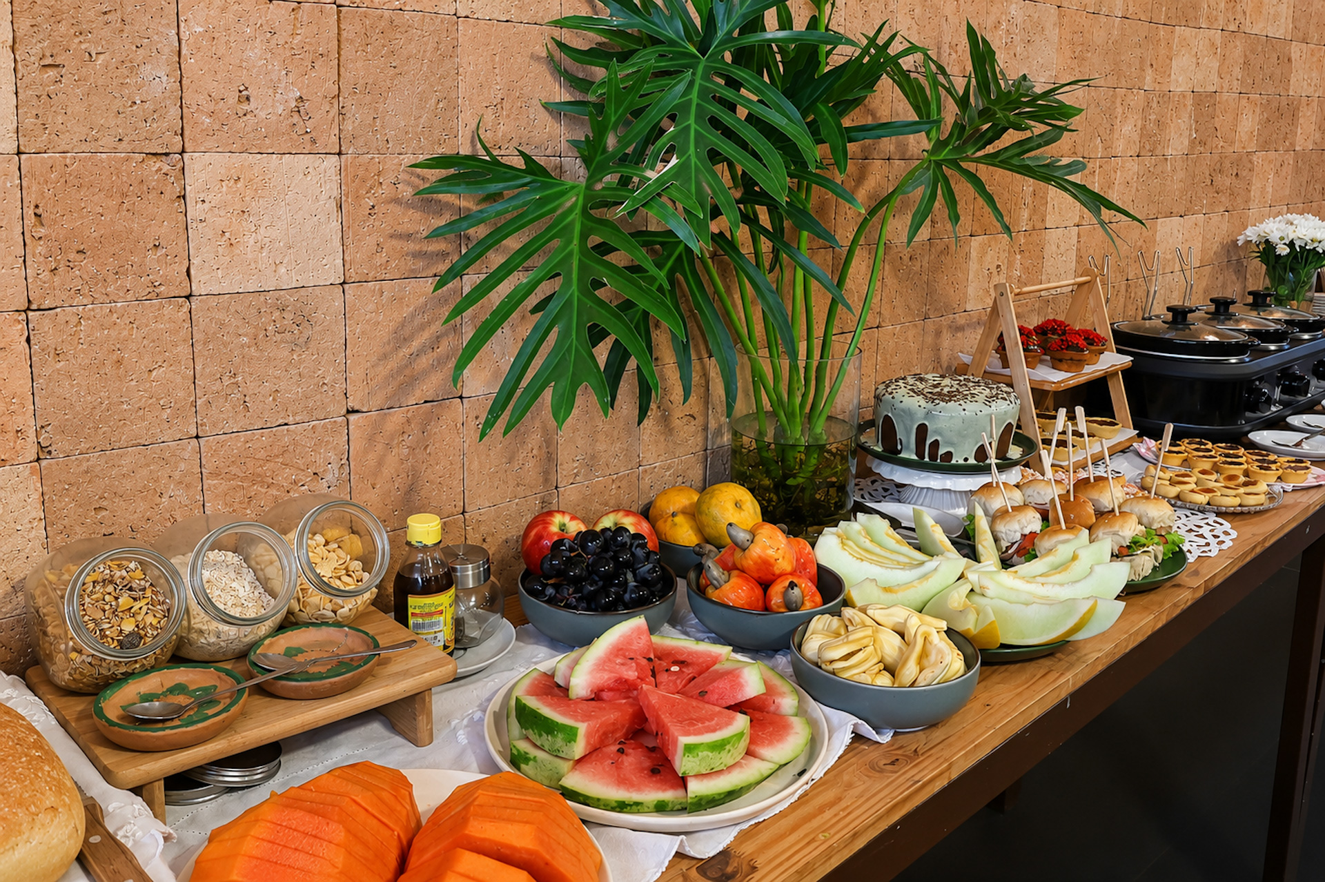 Mesa de café da manhã com frutas variadas (melancia, melão, uva, manga) e queijos